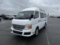 A white 2002 Nissan Van with a boxy design and a high roof featuring large windows and a grille in the front