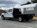 A white 2020 Ford F-350 pickup truck with a flatbed and chrome wheels is parked with its driver's side facing forward