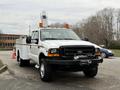 A white 2001 Ford F-350 truck with a flatbed and amber lights on top is parked with a winch on the front and sturdy tires designed for heavy-duty tasks