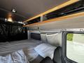 Interior of a 2017 Mercedes-Benz Sprinter with a sleeping area featuring a bed, pillows, and wooden shelving above for storage