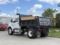 A 2017 Ford F-750 dump truck with a black bed and wooden lining parked with its tailgate down