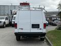 A white 2013 Ford Econoline van parked with a roof rack and no visible license plate on the rear