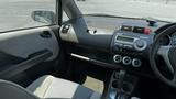 Interior of a 2006 Honda Fit showing the dashboard with control knobs and a gear shift with a gray fabric seat visible