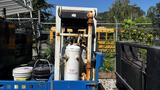 A 2000 Flat Deck 18 Foot truck with a platform holding several gas cylinders and storage containers in a work setting