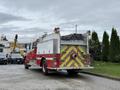 A red and white 2001 Freightliner FL80 fire truck with a hose on the rear and storage compartments on the sides parked with a sign that reads KEEP BACK 150 meters