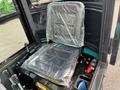 A black seat covered in plastic wrap inside the cab of a 2024 AGT Industrial Green QH13R Mini Excavator with controls and levers visible