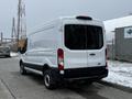 A white 2021 Ford Transit van with a high roof and sliding side door seen from the rear on a snowy street