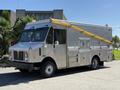 A 2009 Morgan Olson Workhorse W62 food truck with a silver exterior featuring yellow awnings and multiple side compartments