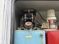 A blue tank with a rusted valve on top and a black air compressor connected to hoses along with a red container labeled Fire-Ball