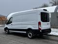 A white 2021 Ford Transit van with a high roof and a black lower trim, viewed from the rear side with no visible markings or logos