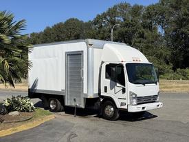 A white 2013 Isuzu NPR box truck with a silver rear cargo door parked on a paved area