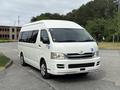 A white 2009 Toyota Hiace van parked on a road with large windows and a sliding side door