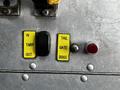 Control panel with yellow buttons labeled IN TARP OUT TAIL GATE and a red light on a metallic surface