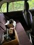 A 1978 Volvo 244 interior featuring faded purple cloth seats with a cluttered back seat area filled with boxes of car parts and tools