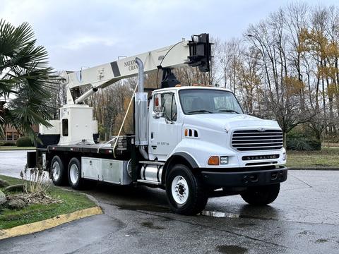 A white 2004 Sterling LT9500 truck equipped with a large aerial lift attached to the back and a flatbed design