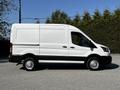 A 2021 Ford Transit van in white with black accents parked on a surface  features a boxy design with sliding side doors and large rear doors