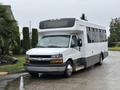 A white 2020 Chevrolet Express shuttle bus with tinted windows and a yellow strip along the bottom parked on a wet surface