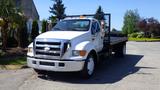 A white 2006 Ford F-650 flatbed truck with orange lights on the roof parked on a street