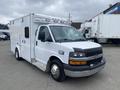 A white 2014 Chevrolet Express van with a boxy shape large front grille and emergency lights on top