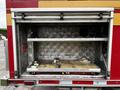 An open compartment of a 2009 Spartan Gladiator fire truck displaying two metal shelves and a wooden platform inside