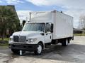 A 2014 International TerraStar box truck with a white exterior and a large cargo area mounted on the back parked on a driveway
