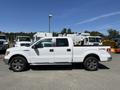 A white 2014 Ford F-150 truck with a crew cab and a utility bed equipped with machinery on the back