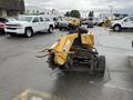A yellow 2014 Vermeer Corporation Sweep Stump Cutter with large wheels and a rotating cutting blade at the front positioned on a paved surface