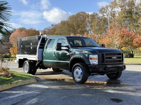 A green 2008 Ford F-550 with a flatbed and tool storage compartment is parked with its wheels on a wet surface. It features a crew cab design with a double cabin layout.