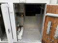 An open storage compartment in a 2005 Freightliner M2 106 with metal walls and a small electrical box inside