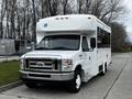 A white 2016 Ford Econoline bus with a wheelchair access symbol on the front and large windows on the side