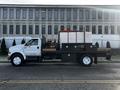 A white 2011 Ford F-750 flatbed truck with a black cab and utility boxes on the side, carrying equipment and containers in the truck bed