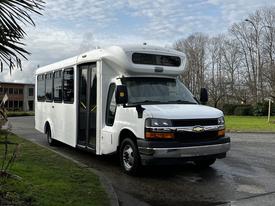 A 2015 Chevrolet Express bus in white with a front entrance door and large windows