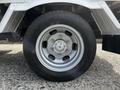 Close-up of a silver alloy wheel featuring a six-bolt pattern mounted on a 2004 Toyota Toyoace with a black tire featuring a tread pattern