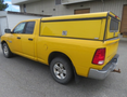 A yellow 2015 RAM 1500 pickup truck with a fitted cap on the bed and silver rims visible from the rear and side angle