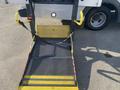 A yellow and black wheelchair lift with a mesh platform and safety straps is shown, positioned for use on a vehicle