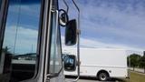 A 2011 Ford Econoline with a focus on its side mirror and window reflecting the sky in the background