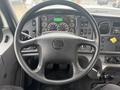 A black steering wheel with a central logo and multiple gauges on a dashboard including speedometer and various control buttons of a 2016 Freightliner 108SD