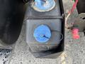 A close-up of a blue cap on a black fluid reservoir mounted on a vehicle with a visible wiring connection and part of the vehicle frame