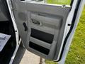 The image shows the driver side door of a 2019 Ford Econoline featuring a gray interior handle and armrest with a textured panel and storage compartment