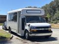 A 2020 Chevrolet Express shuttle bus with a white exterior parked on the side of the road featuring large tinted windows and a black front grille