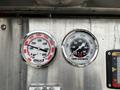 Two pressure gauges mounted on a metal panel showing readings for vacuum and pump discharge with numerical markings and colored dials