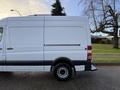 A white 2012 Mercedes-Benz Sprinter van is pictured from the side showcasing its high roof and large cargo area with black trim on the lower body