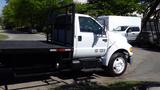 A white 2006 Ford F-650 truck with a flatbed and a black mesh side rail visible from the driver’s side showcasing its large tires and sturdy frame