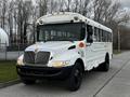 A white 2013 International 4200 school bus with black wheels and multiple lights on the roof facing forward