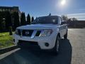 A white 2015 Nissan Frontier is parked in the foreground showcasing its front grille headlights and body design