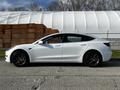 A 2019 Tesla Model 3 in white parked on a concrete surface with a sleek design and sporty black wheels