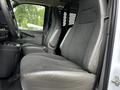 Interior view of a 2023 GMC Savana showing two gray fabric seats with a console and a metal partition visible between the seats