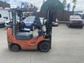 A 2010 Toyota 7FGGU25 forklift with an orange and gray body and a black lifting mechanism parked on a lot among vehicles