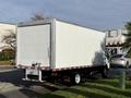 A white 2018 Hino 195 box truck with a rear roll-up door and reflective striping on the bumper parked on a grassy area