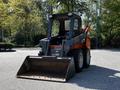 A 2017 Gehl R105 skid steer loader with a front bucket and a black and orange color scheme parked on a paved surface